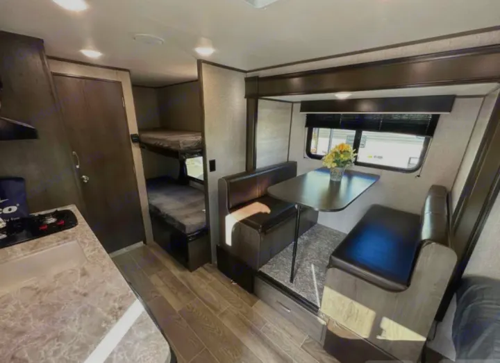 Rv rental interior: on the left, a galley kitchen and bunk beds. On the right, a dinette with bench seating, a table, and a window.. Jayco Jay Flight SLX 2021