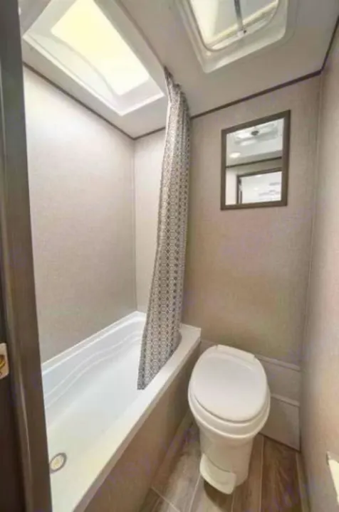 Compact RV rental bathroom featuring a bathtub/shower with curtain, toilet, and mirror. Ideal for travel trailer adventures.. Jayco Jay Flight SLX 2021