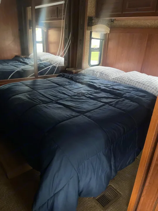Comfortable RV rental bedroom. Features a large bed with dark blue comforter, grid pillows, and mirrored wardrobe.. Forest River Other 2014