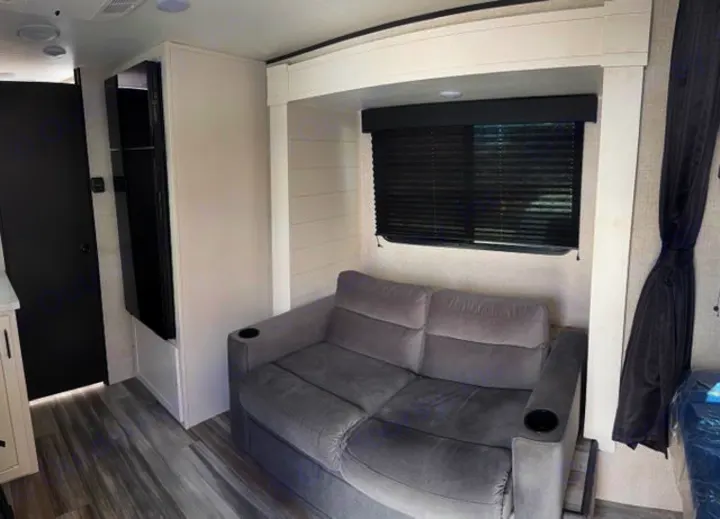 Inviting RV rental interior with gray sofa, window, light flooring, and a narrow fridge/pantry unit.. JAYCO Jay Flight 2025