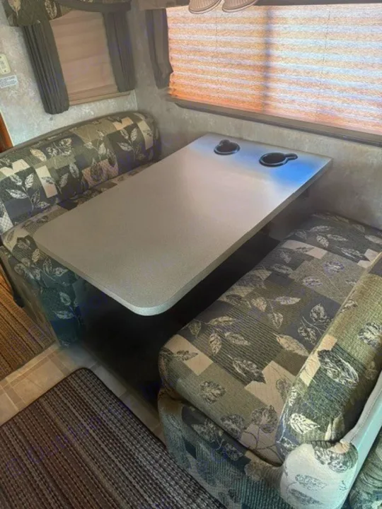 Cozy RV rental dinette featuring patterned booth seating and a table with built-in cup holders.. Coachmen Mirada Deluxe/Premier 2004