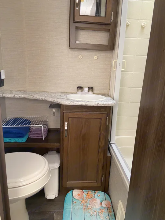 This RV rental features a functional bathroom, complete with a white toilet, sink vanity, and shower. Towels and storage are visible.. Keystone RV Bullet Crossfire 2018