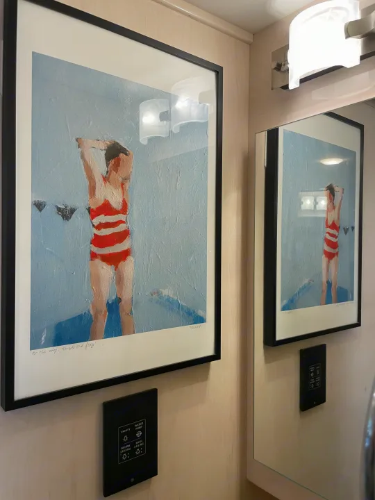 Framed art of a swimmer hangs on a light wood wall in this RV rental, with a control panel and mirror visible.. Renegade Custom Coaches Vienna 2021