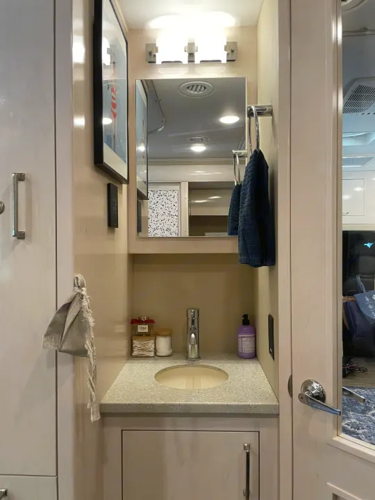 Inside a cozy RV rental: a compact bathroom vanity with sink, mirror, bright lights, and organized toiletries.. Renegade Custom Coaches Vienna 2021