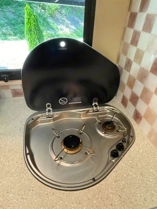 Inside an RV rental: a Dometic two-burner stove with its lid open, showing stainless steel. Perfect for camping cooking.. Renegade Custom Coaches Vienna 2021