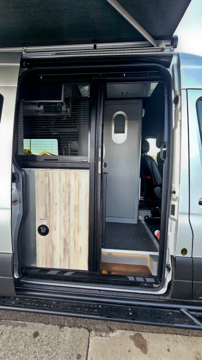Inside an RV rental camper van: The open side door reveals a custom interior with a window, sink, and unique gray door.. Airstream Interstate 2024