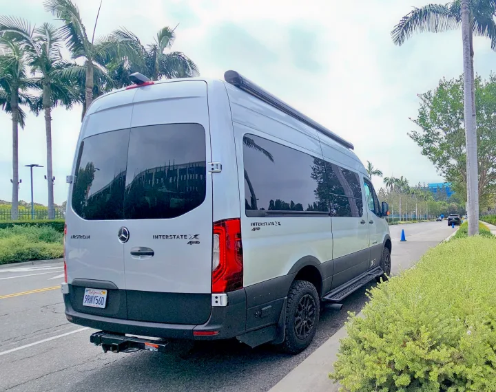 A light gray Airstream Interstate X 4x4 rv rental parked curbside with palm trees. California license plate.. Airstream Interstate 2024