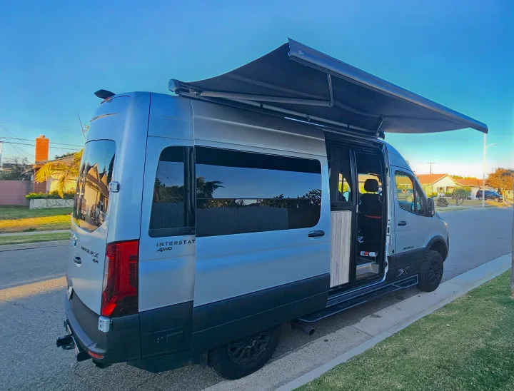 Explore in style with this silver camper van RV rental, featuring a side awning for shade.. Airstream Interstate 2024