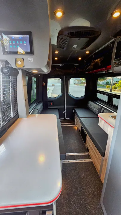 Interior of a modern rv rental van showing a bright dinette table, dark bench seats, smart lighting controls, and overhead AC.. Airstream Interstate 2024