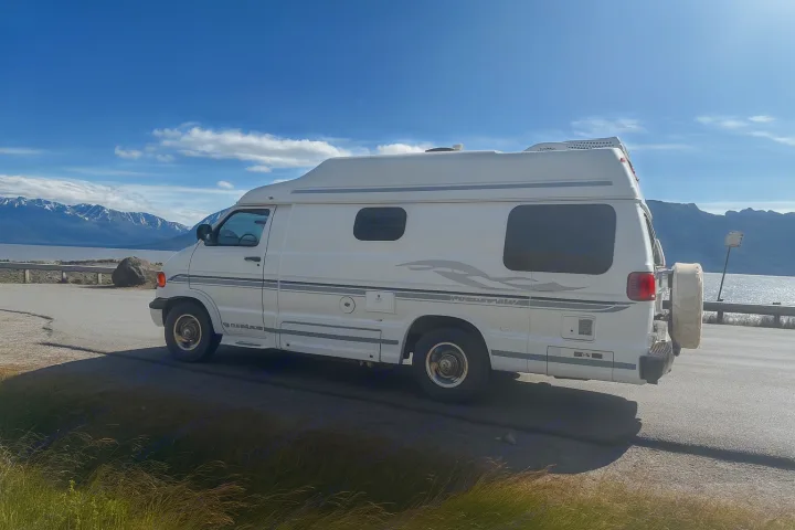 White RV parked by a scenic lake and mountains. An ideal rv rental for exploring beautiful landscapes.. Pleasure Way Excel 2001