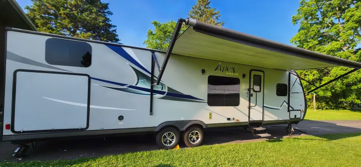 This Apex Ultra Lite travel trailer, ready for an RV rental adventure, features an extended awning in a sunny outdoor setting.. Coachmen Apex 2018