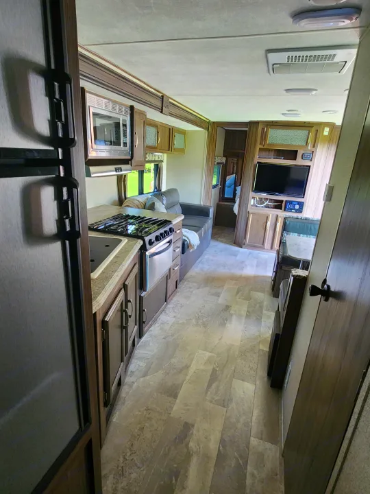 Spacious RV rental interior featuring a modern kitchen, living area with TV, and clean wood-look flooring.. Coachmen Apex 2018