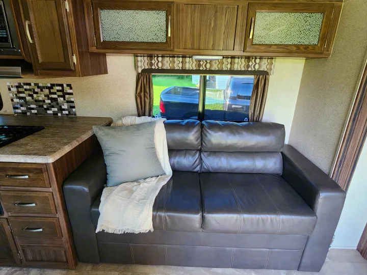 RV rental interior: cozy leather sofa with pillow/throw, kitchen area, and wood cabinetry. Ready for your adventures.. Coachmen Apex 2018