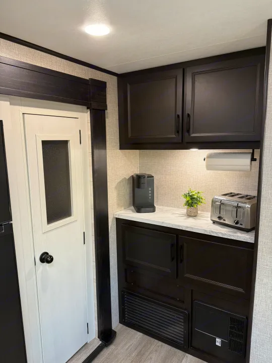 Modern RV rental kitchen with black cabinets, white counters, Keurig, toaster, and pantry door. Bright interior.. Jayco Jay Flight 2022