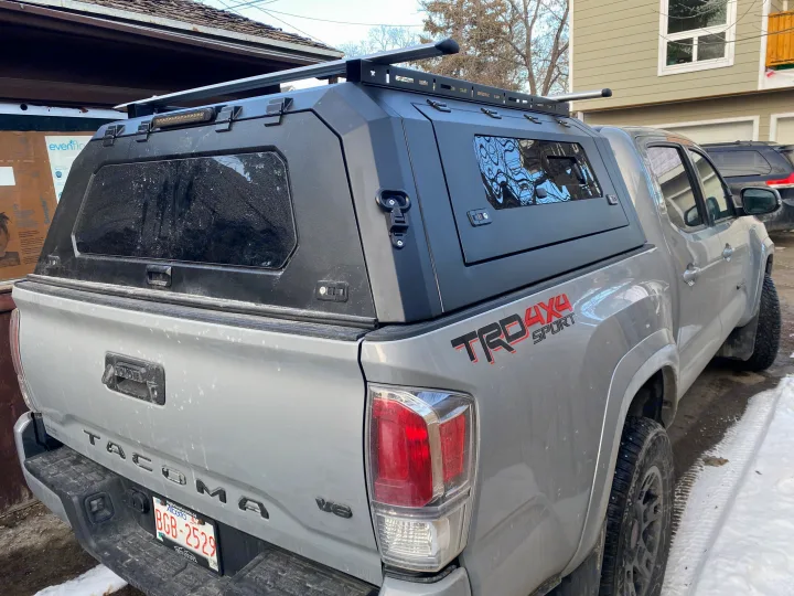 Rugged grey Toyota Tacoma pickup with a hard camper shell & roof rack for overlanding. Perfect alternative to RV rental.. Toyota Tacoma 2020