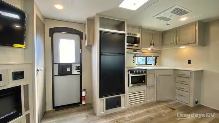 RV rental interior: a light kitchen with fridge, stove, microwave, and cabinets. Living area with TV and entry door visible.. Coachmen Catalina Legacy Edition 2022
