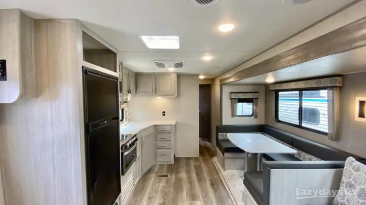 Modern RV rental interior: well-lit kitchen and dining booth with light wood finishes.. Coachmen Catalina Legacy Edition 2022