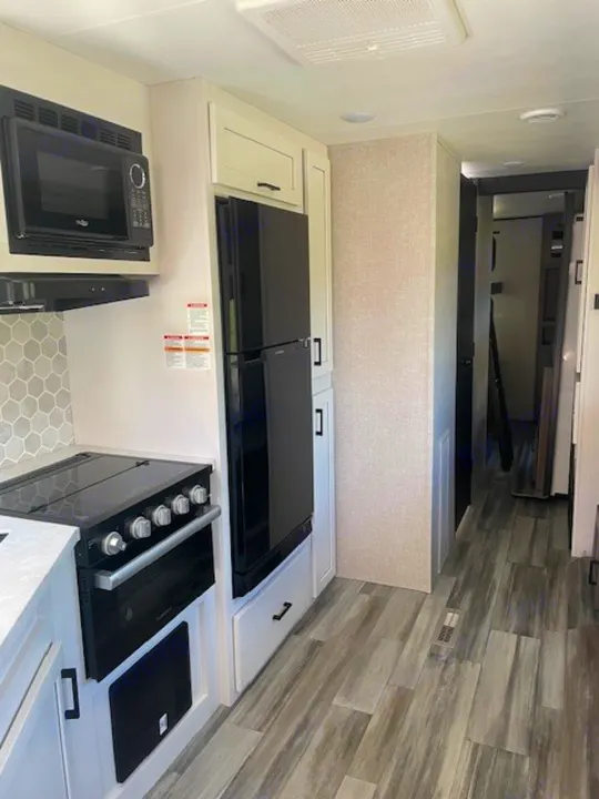 Spacious RV rental kitchen featuring a microwave, stove, fridge, and stylish wood-look flooring leading to a hallway.. Jayco Jay Flight SLX 2024