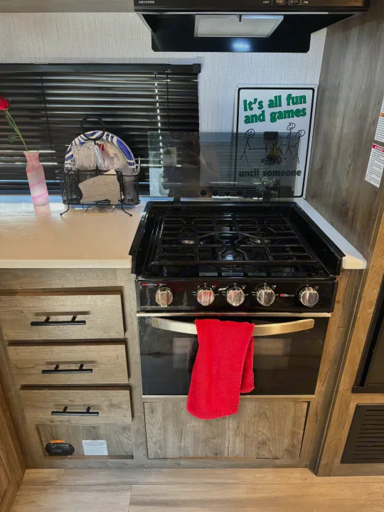 RV rental kitchen features a gas stove/oven, countertop, a red towel, and a humorous sign above the range.. Heartland RVs Pioneer 2022