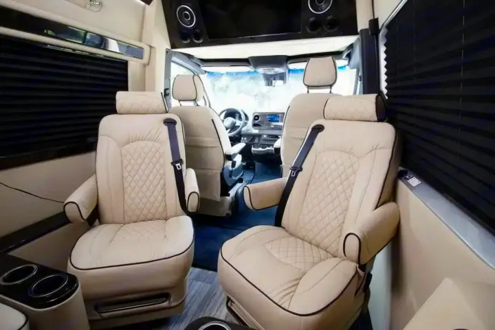 Plush RV rental interior showcasing two cream, quilted captain's chairs, cupholders, and privacy blinds.. Ultimate Toys Ultimate Cruiser 2024