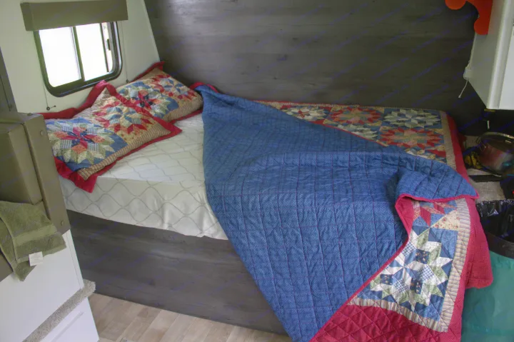 Inside an RV rental, a cozy bedroom with a bed adorned with colorful, patterned quilts and pillows, beside a window.. Keystone RV Hideout 2022