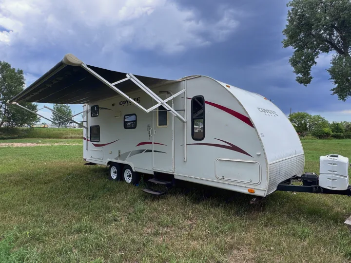 White Coyote Lite travel trailer, awning extended, parked on green grass. Consider this spacious RV rental for your next camping trip.. kz Coyote 2010