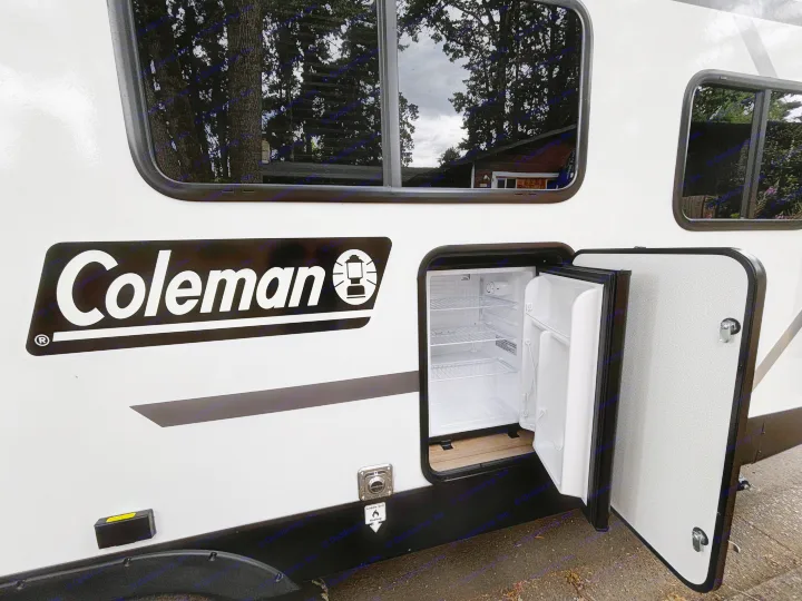 This RV rental features a convenient outdoor mini-fridge, seen open with shelves, and a grill hookup on a Coleman RV.. Keystone Coleman Light 2026