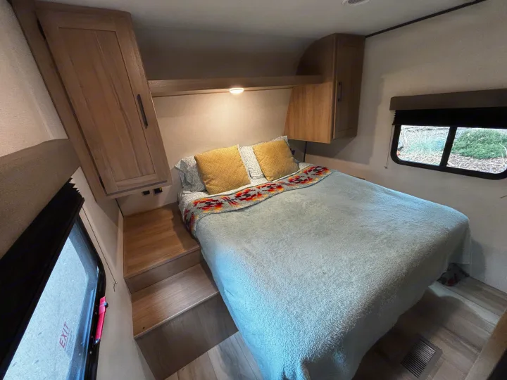 Cozy RV rental bedroom featuring a comfortable bed with steps, built-in wooden cabinetry, and a window with blinds.. Keystone Coleman Light 2026