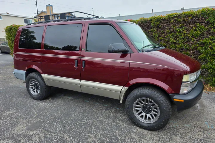 Maroon and tan Chevy Astro van, equipped with a roof rack and all-terrain tires. Perfect for your next RV rental adventure.. Chevrolet Astro 2003