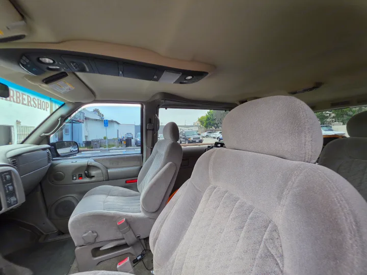Inside an RV rental van: light grey fabric seats, overhead console, and view of a barbershop outside.. Chevrolet Astro 2003