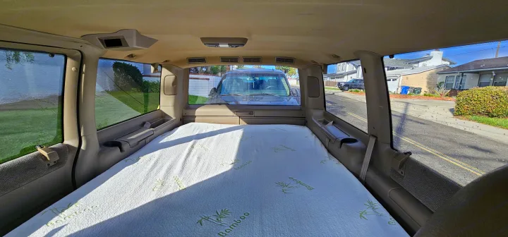 Interior of an RV rental showing a bamboo mattress set up for sleeping, with a view of a residential street outside.. Chevrolet Astro 2003