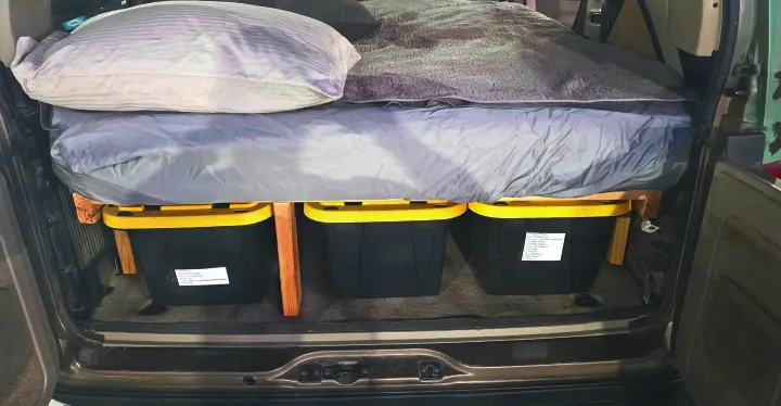 Efficient car camping setup in an RV rental with an elevated bed and labeled storage bins for gear.. Chevrolet Astro 2003