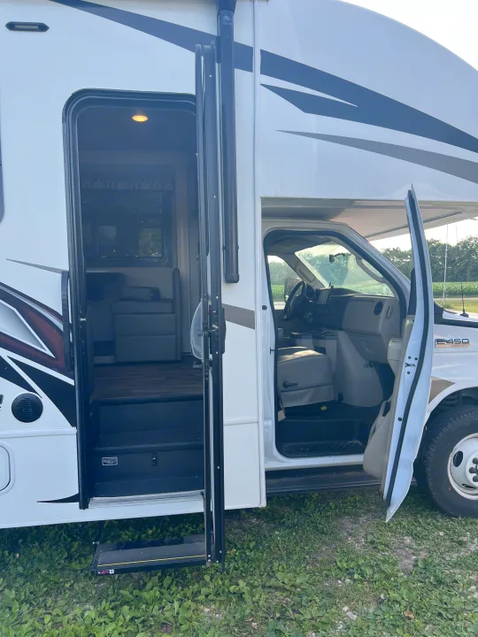 Open doors of a white RV rental, showing the inviting interior with steps and the driver's area. Start your journey!. Jayco Redhawk 2021