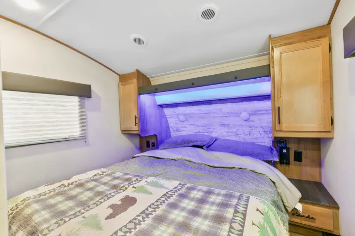 RV rental bedroom with a cozy bed, nature-themed comforter, overhead storage, and ambient purple lighting for your travels.. Cherokee limited Arctic Wolf 2023