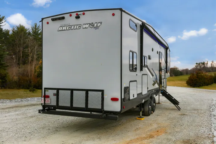 Rear view of a gray Arctic Wolf toy hauler RV rental on gravel. Features include a cargo ramp, blue awning lights, and steps.. Cherokee limited Arctic Wolf 2023