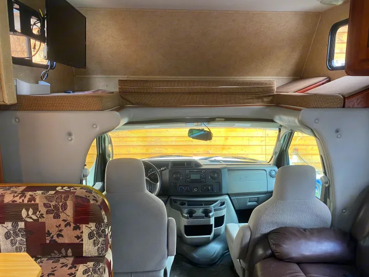 Spacious RV rental interior: view from living area towards the cockpit, revealing front seats, dashboard, and an overhead bunk.. Forest River Sunseeker 2011