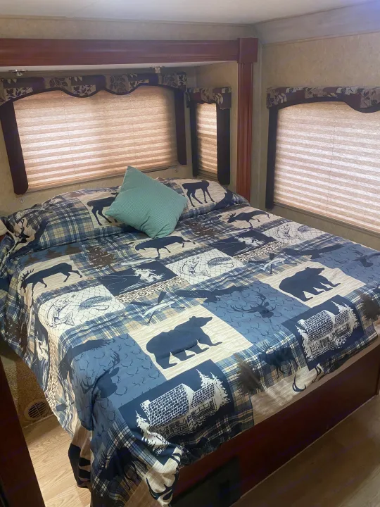 Cozy RV rental bedroom with nature-themed comforter (bears, deer, fish) & privacy blinds for a peaceful stay.. Forest River Sunseeker 2011