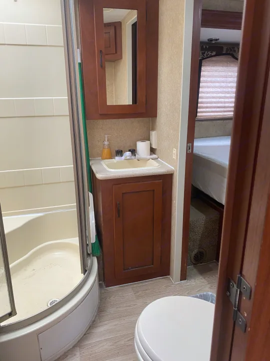 This RV rental's compact bathroom features a corner shower, sink vanity, and toilet, with a glimpse into the bedroom.. Forest River Sunseeker 2011