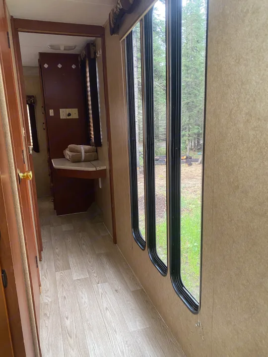 An RV rental's cozy interior, showing a hallway, open door to another room, and tall windows with a peaceful forest view.. Forest River Sunseeker 2011
