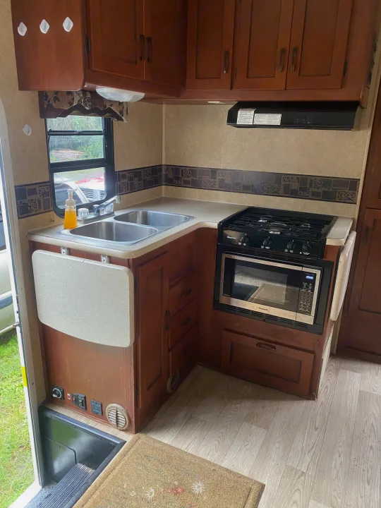 This RV rental kitchen features a double sink, stovetop, microwave, and ample cabinets, perfect for your road trip camper.. Forest River Sunseeker 2011