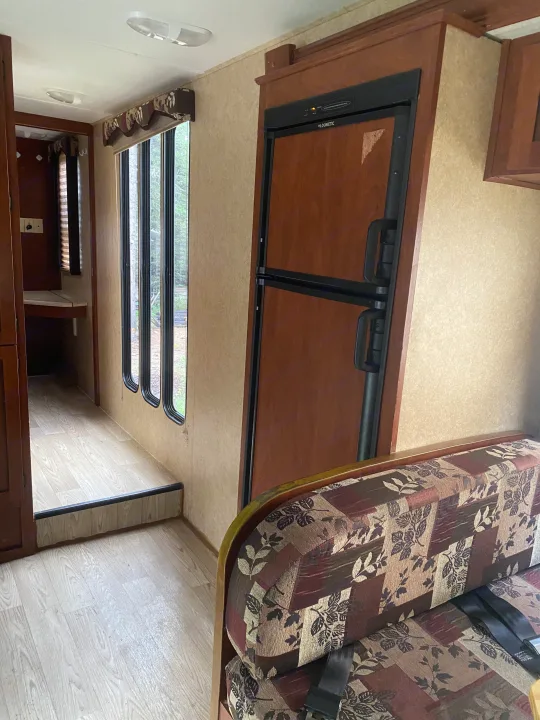 RV rental interior: shows a Dometic fridge, upholstered dinette with seatbelts, and windows overlooking nature.. Forest River Sunseeker 2011