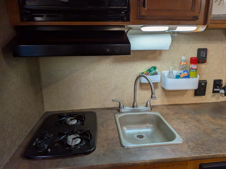 RV rental kitchen featuring a compact stove, sink, microwave hood, and cooking/cleaning supplies. Perfect for travel.. Starcraft AR-One 2015