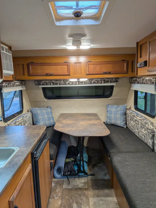 Cozy RV rental interior showcasing a dinette, compact kitchen with sink, and wooden overhead cabinets.. Starcraft AR-One 2015