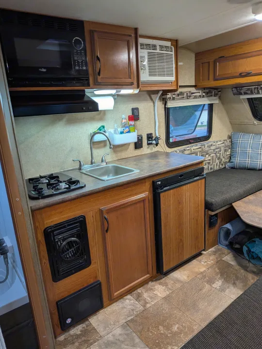 Compact RV rental kitchen area: microwave, stovetop, sink, fridge, AC, and dinette seating. Ready for travel.. Starcraft AR-One 2015