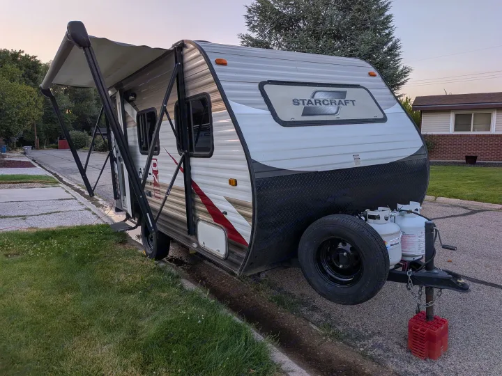 A StarCraft RV rental travel trailer is parked curbside with its awning extended and propane tanks visible.. Starcraft AR-One 2015