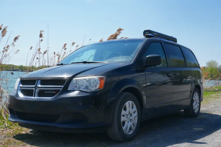 Black Dodge Grand Caravan minivan with a Yakima RoadShower by water. A great RV rental option for a versatile camper van adventure.. Dodge Grand Caravan 2014