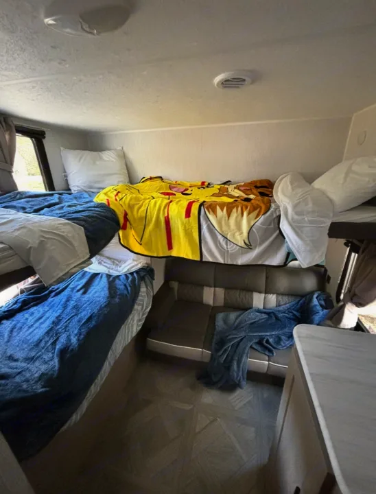 An RV rental's comfy bunk bed setup, featuring a vibrant Pikachu blanket, a lower bed, and a compact seating area.. Forest River Wildwood X-Lite 2024