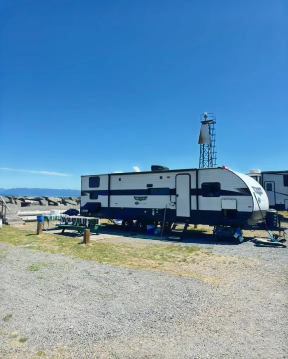 RV rental parked at a sunny coastal campground, showcasing ocean views, rocky shore, and distant mountains under a clear blue sky.. Forest River Wildwood X-Lite 2024