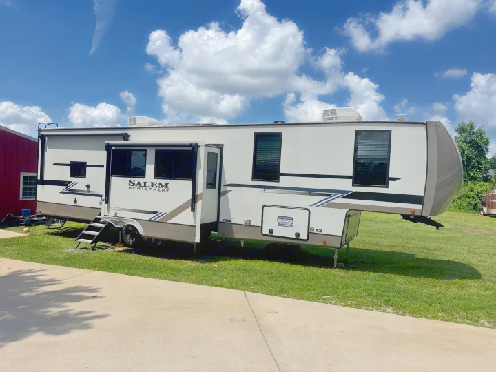 White and gray Salem Hemisphere fifth-wheel RV is parked on grass with slides out, perfect for your next RV rental adventure.. Forest River Salem Hemisphere 2024