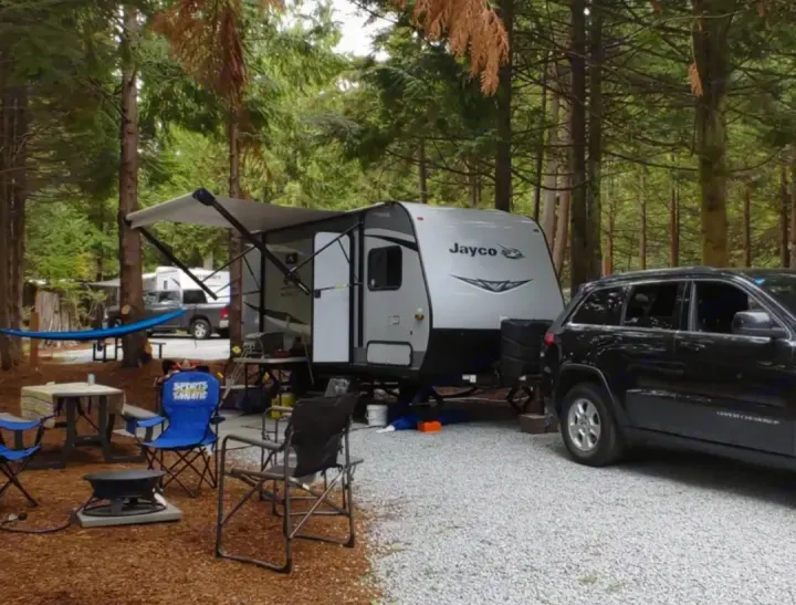 This RV rental provides comfort in nature. A Jayco travel trailer with awning, SUV, chairs, and hammock at a serene campsite.. Jayco Jay Flight 2021